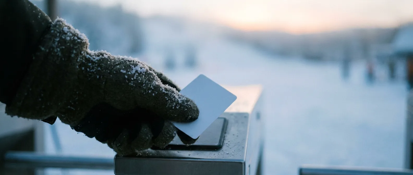 En hand i vante håller ett liftkort mot kortläsaren vid en grind